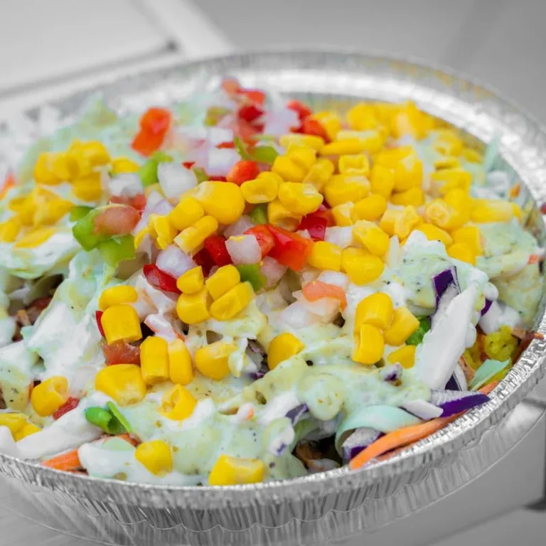 Close-up of a Mambo Cari-Bowl topped with corn, pico de gallo, slaw, and green sauce.