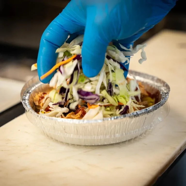 Mambo team member preparing a Cari-Bowl with fresh slaw inside the food truck.