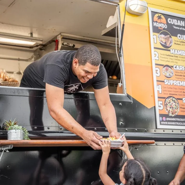 Mambo team member handing a prepared meal to a guest from the Cuban food truck.